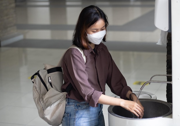 Jonge vrouwelijke universiteitsstudent die masker draagt en handen wast tijdens covid19