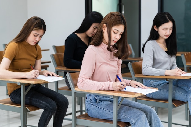 Jonge vrouwelijke universiteitsstudenten concentreren zich op het doen van examen in de klas. Meisjesstudenten schrijven serieus de oefening van de examens in de klas.