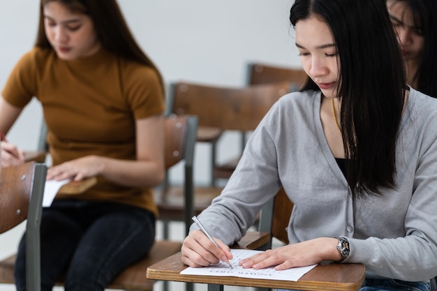 Jonge vrouwelijke universiteitsstudenten concentreren zich op het doen van examen in de klas. Meisjesstudenten schrijven serieus de oefening van de examens in de klas.