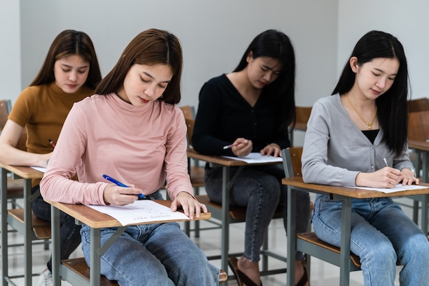 Jonge vrouwelijke universiteitsstudenten concentreren zich op het doen van examen in de klas. Meisjesstudenten schrijven serieus de oefening van de examens in de klas.