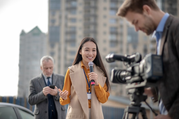 Jonge vrouwelijke verslaggever in een beige outfit praten met een camera