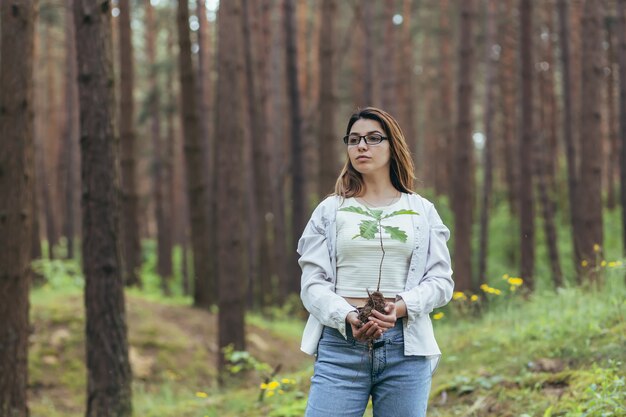 Jonge vrouwelijke vrijwilliger plant een bos en houdt een zaailing van een eikenboom in haar handen