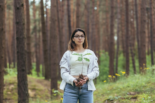 Jonge vrouwelijke vrijwilliger plant een bos en houdt een zaailing van een eikenboom in haar handen