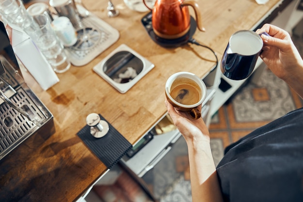 Jonge vrouwelijke vrouwenbarista die verse melk gieten om latte-koffie voor klant in koffie voor te bereiden.