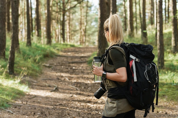 Jonge vrouwelijke wandelaar met grote rugzak en herbruikbare fles voor water in groen bos