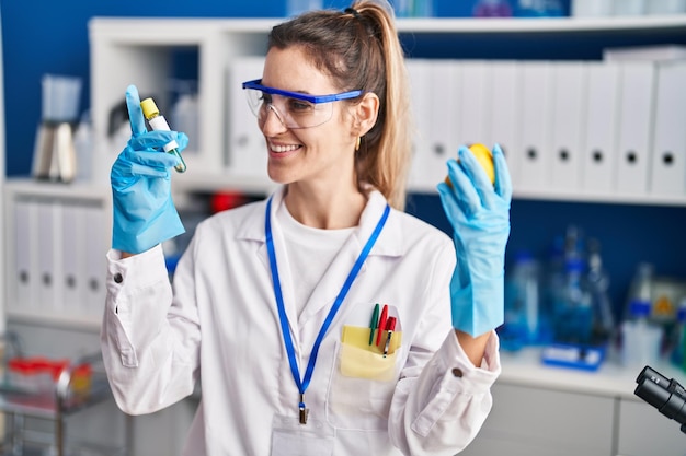 Jonge vrouwelijke wetenschapper die reageerbuis en citroen vasthoudt in het laboratorium