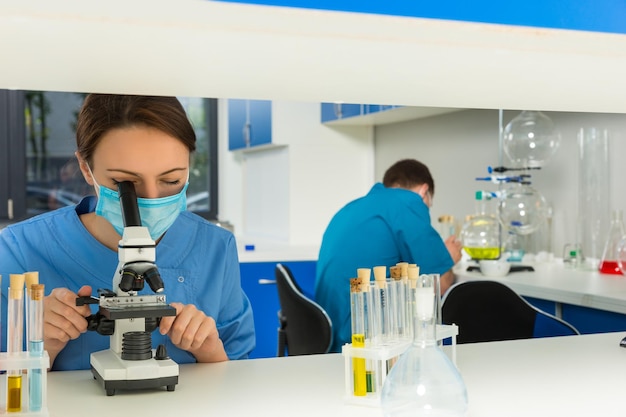 Foto jonge vrouwelijke wetenschapper in uniform kijkt door een microscoop en mannelijke wetenschapper doet wat onderzoek in een laboratorium op een achtergrond. gezondheidszorg en biotechnologie concept