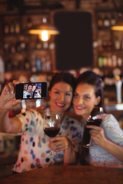 Jonge vrouwen die een selfie nemen vanaf de mobiele telefoon terwijl ze een rode wijn drinken