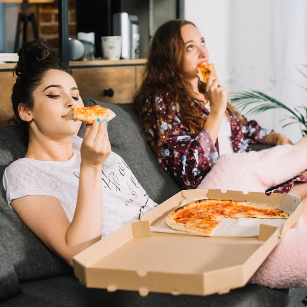 Jonge vrouwen die op bank zitten die pizza eet