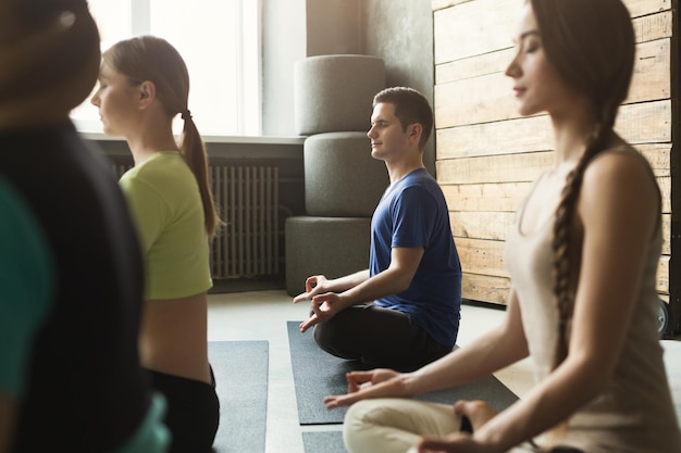 Jonge vrouwen en man in yogales, meditatieoefeningen. Lotus pose voor ontspanning. Gezonde levensstijl in fitnessclub, bijsnijden, kopieerruimte, selectieve focus