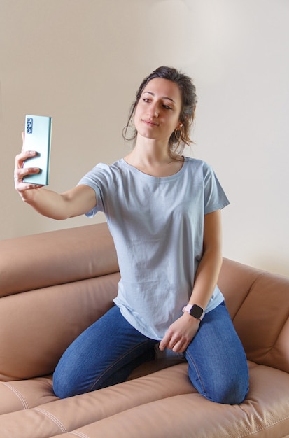 Jonge vrouwen in glazen en blauw t-shirt die selfie met celtelefoon thuis nemen