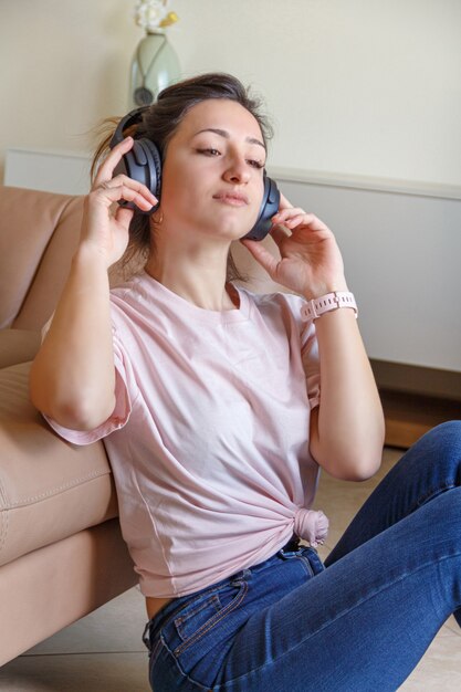 Jonge vrouwen luisteren naar muziek met een koptelefoon terwijl ze thuis in de buurt van de beige bank zitten