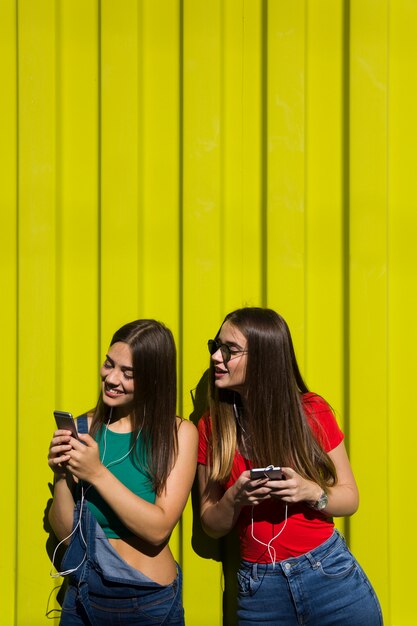 Jonge vrouwen openlucht tegen gele muur luisteren muziek op hoofdtelefoons en hebben pret