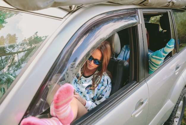 Jonge vrouwen rusten met haar benen over een auto met open raam. Reis en ontspan tijdconcept.