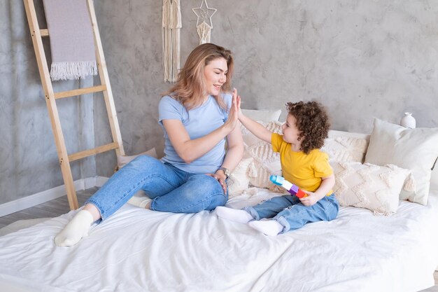 Jonge vrouwen spelen met haar gekrulde dochter op bed, ze lachen knuffelen en hebben samen plezier