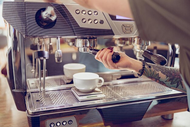 Jonge vrouwenbarista die koffiemachine in koffiehuis gebruikt