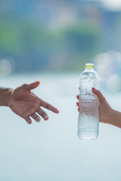 Jonge vrouwenhand die of een fles vers koud drinkwater aan een mens na geschiktheidsoefening geeft dient.