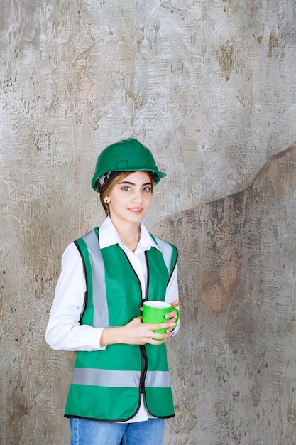 Jonge vrouweningenieur die een groen vest draagt en een koffiekop houdt