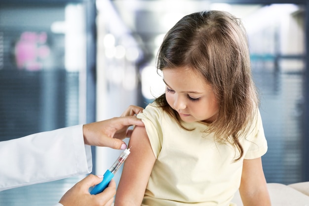 Jonge vrouwenkinderarts die vaccinatie van een klein meisje doet