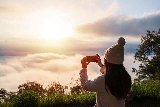 Jonge vrouwenreiziger die foto met slimme telefoon neemt op zee van mist en zonsopgang boven de berg