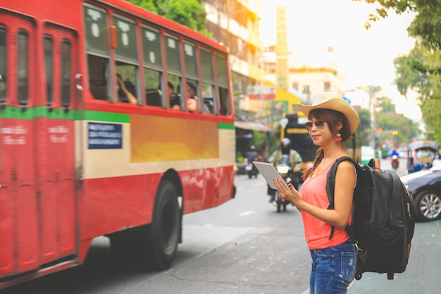 Jonge vrouwenreiziger die met zwarte rugzak en hoed kaart op de tablet in bangkok bekijken. reizen concept