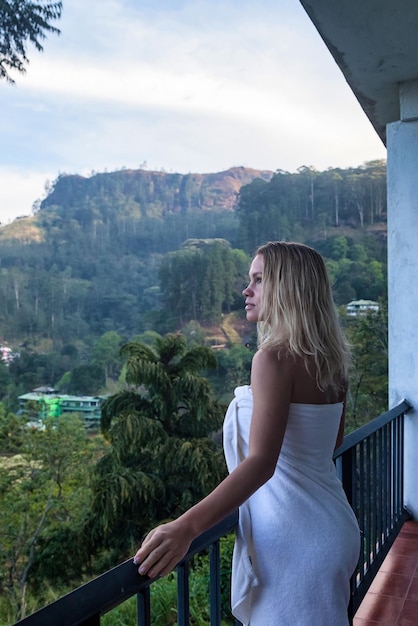 Jonge vrouwenreiziger die zich op hotelbalkon bevindt en berglandschap bekijkt platteland