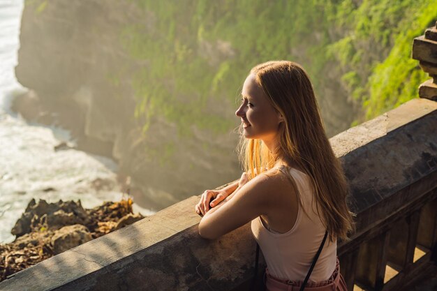 Jonge vrouwenreiziger in de tempel van Pura Luhur Uluwatu, Bali, Indonesië. Geweldig landschap - klif met blauwe lucht en zee.