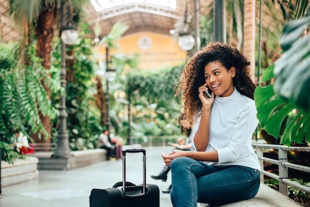 Jonge vrouwenreiziger met haar bagage die op telefoon spreekt.