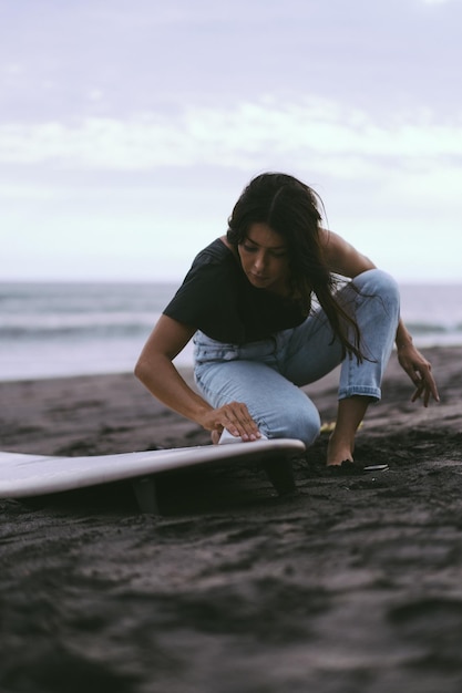 Jonge vrouwensurfer die een surfplank op het in de was zetten van de oceaan voorbereiden Vrouw met surfplank op de oceaan actieve levensstijl watersporten