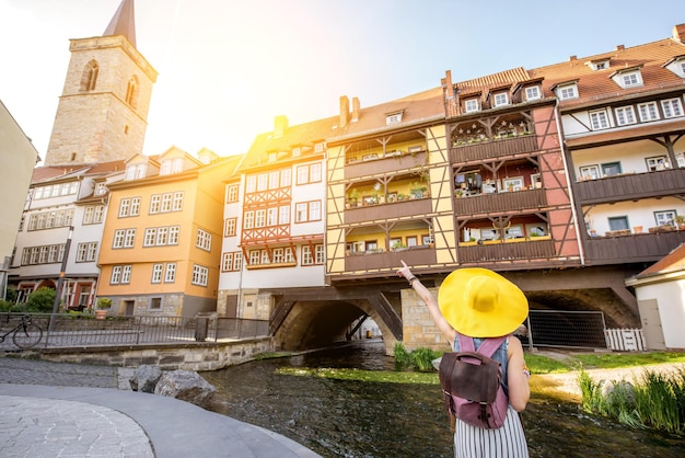 Jonge vrouwentoerist met gele hoed die achterover staat op de beroemde Merchants bridge-achtergrond in de stad Erfurt, Duitsland