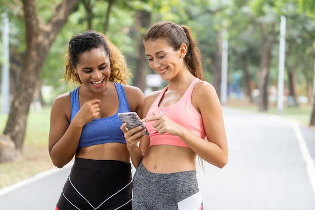 Jonge vrouwenvrienden die samen bij park joggen. Vrouwelijke lopers luisteren naar muziek tijdens het joggen.