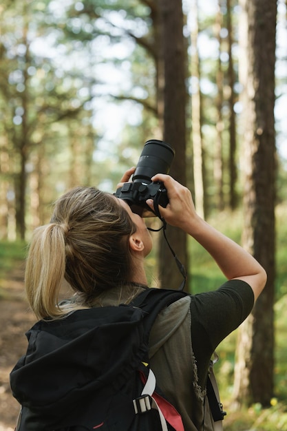 Foto jonge vrouwenwandelaar met het nemen van foto's met een moderne spiegelloze camera in groen bos.