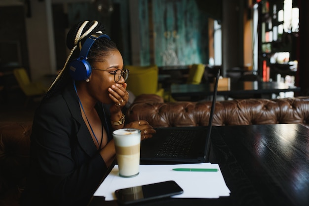 Jonge vrouwenzitting in een koffie die aan laptop werkt