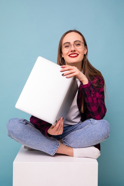 Jonge vrouwenzitting met laptop op blauwe achtergrond