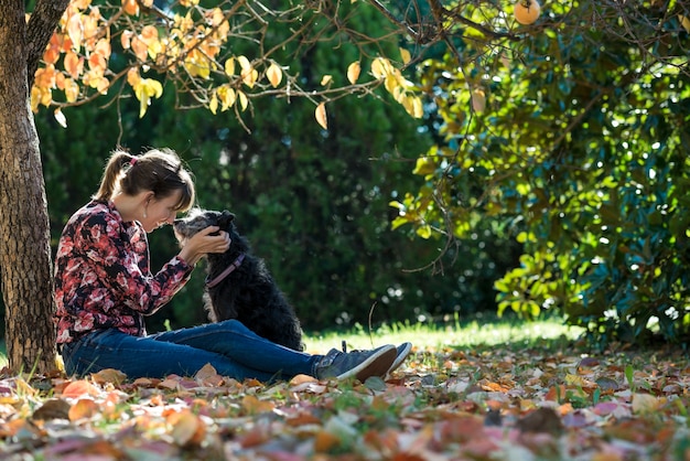 Jonge vrouwenzitting onder een coulourful autumboom die veel liefs haar zwarte hond aaien