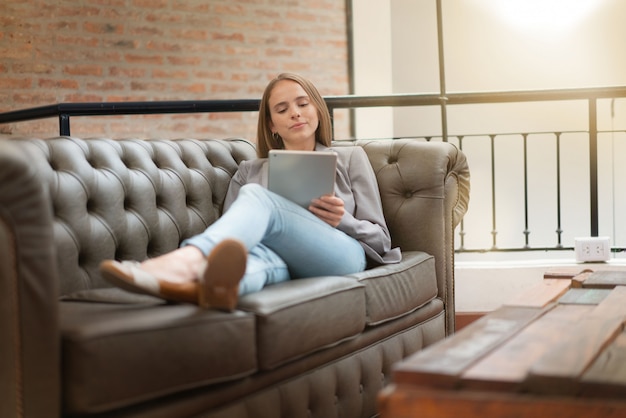 Jonge vrouwenzitting op bank die in modern bureau werkt