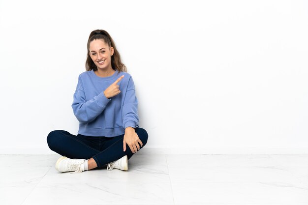 Jonge vrouwenzitting op de vloer die aan de kant richt om een product voor te stellen