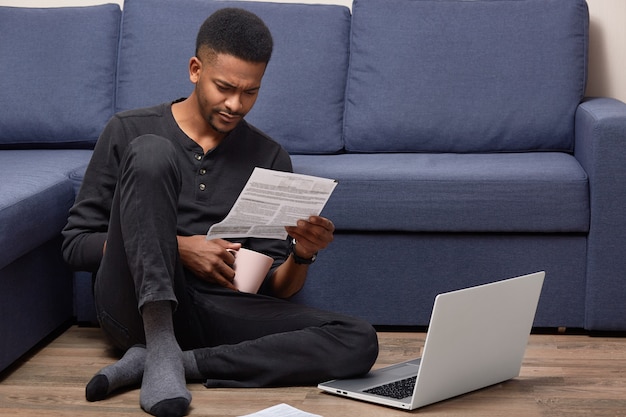 Jonge, welvarende zwarte ondernemer heeft aandachtig naar document gekeken, bestudeert contractvoorwaarden, draagt vrijetijdskleding