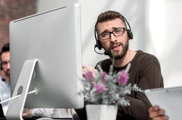 Jonge werknemer in de headset zit aan een tafel in het zakencentrum