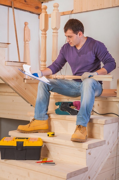 Jonge werknemer zittend op een houten ladder en loking in blauwdruk