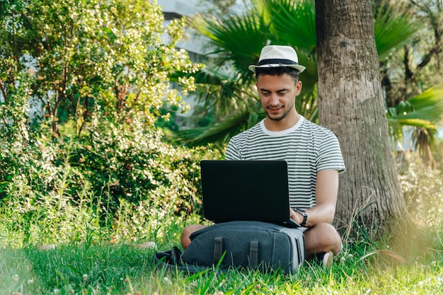 Jonge witte digitale nomade die op afstand werkt met een laptop in een park