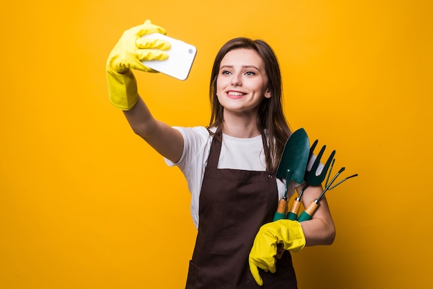 Jonge womang ardener neemt selfie aan de telefoon terwijl hij gereedschap geïsoleerd houdt