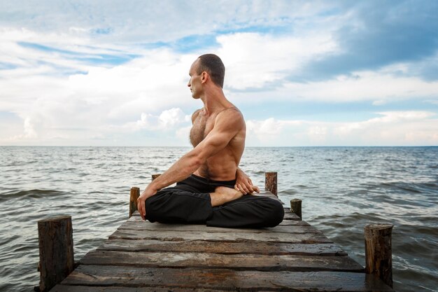 Jonge yogatrainer die yoga-oefeningen doet op een houten pier aan de kust van zee of rivier