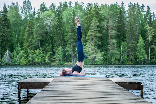 Jonge yogi meisje beoefenen van yoga staande in salamba sarvangasana oefening ondersteund schouder stand pose op het meer concept van gezond leven en natuurlijk evenwicht