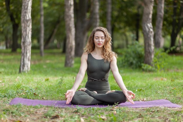 Jonge yogi-vrouw met krullend haar mediteert zittend op een mat in het bos Harmony Healthy lifestyle