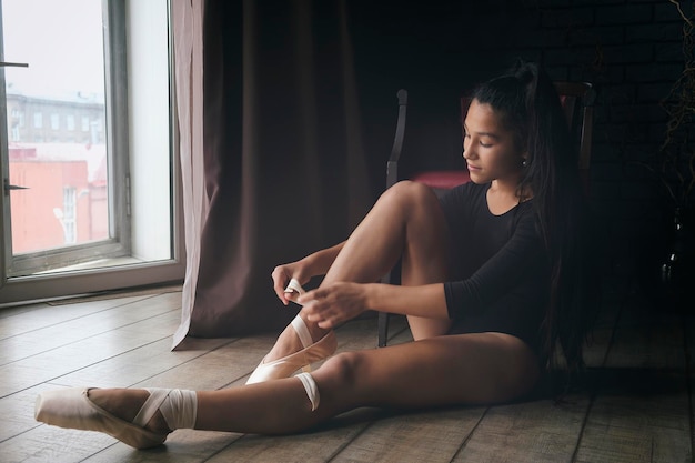 Jonge zachte en bedachtzame ballerina poseert in het interieur en bij het raam