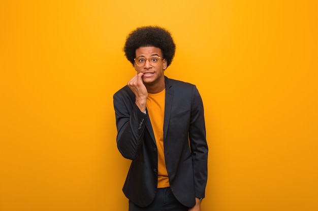 Jonge zakelijke Afro-Amerikaanse man over een oranje muur nagels te bijten, nerveus en erg angstig