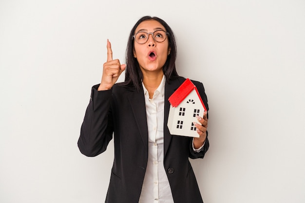 Jonge zakelijke Latijns-vrouw met een speelgoed huis geïsoleerd op een witte achtergrond wijzend ondersteboven met geopende mond.