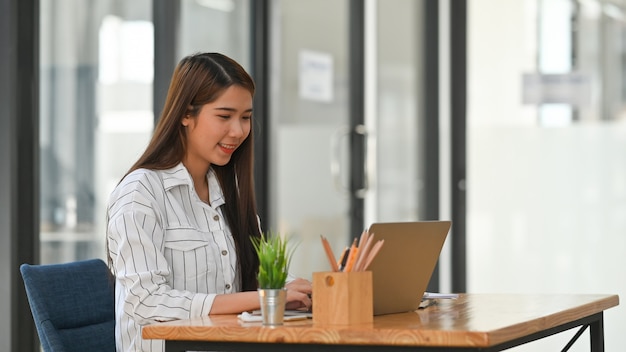 jonge zakelijke meisje in gestreept shirt te typen op de laptop en zit aan de houten bureau