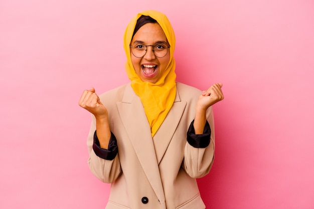 Jonge zakelijke moslimvrouw geïsoleerd op roze muur zorgeloos en opgewonden juichen. Overwinning concept.